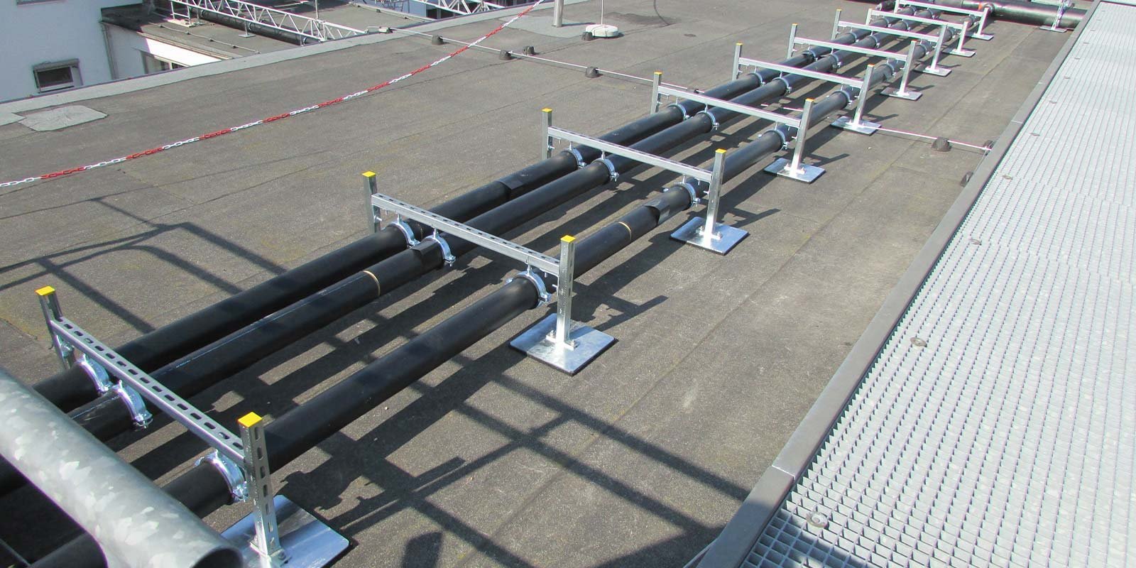 Ein Blick auf das Dach mit mehreren langen, schwarzen Rohren, die ordentlich auf einem grauen Untergrund angeordnet sind.