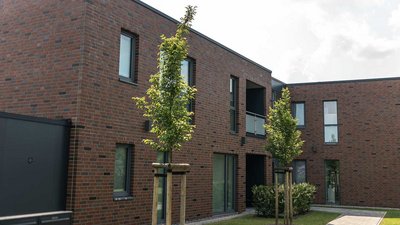 Die Fassade eines modernen Hauses mit klaren Linien, großen Fenstern und einer einladenden Umgebung aus Rasen und Bäumen.