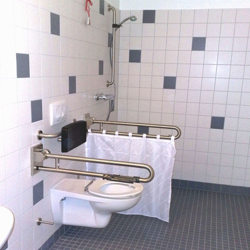 Ein barrierefreies Badezimmer mit einem Toilettenstuhl und Haltegriffen, um die Nutzung zu erleichtern.