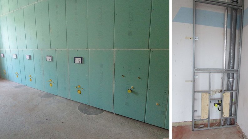 Der Raum zeigt eine unvollendete Wand mit Gipskartonplatten und sichtbaren Rohren für Wasser und Elektrizität.