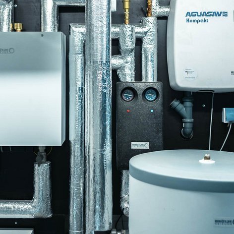 Eine moderne Heizungsanlage mit silbernen Rohren und einem großen Wassertank, die in einem technischen Raum installiert ist.
