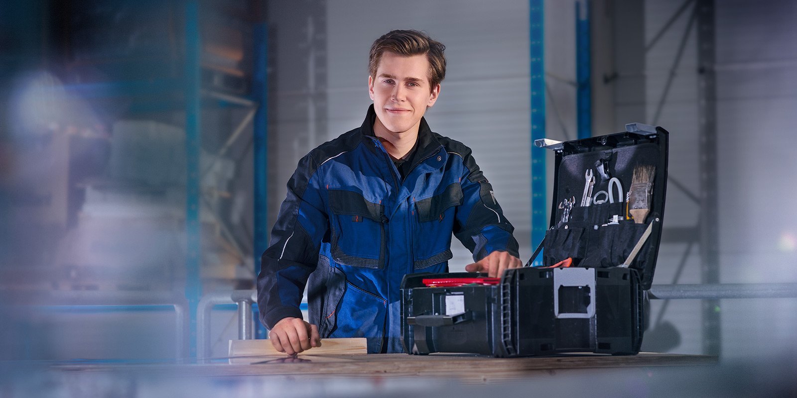 Ein junger Mann in Arbeitskleidung steht an einer Werkbank