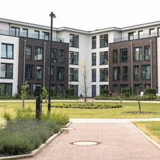 Die Architektur der Wohngebäude ist zeitgemäß, umgeben von einer grünen Landschaft mit Wegen und Sitzgelegenheiten.