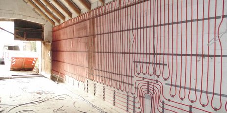 Die Installation von Heizungsrohren an einer Wand in einem Baustellenbereich, mit sichtbarem Schutt und Werkzeugen auf dem Boden.