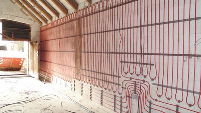 Die Installation von Heizungsrohren an einer Wand in einem Baustellenbereich, mit sichtbarem Schutt und Werkzeugen auf dem Boden.