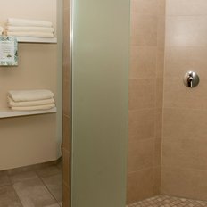 In einem eleganten Badezimmer stehen gefaltete Handtücher auf einem weißen Regal, während die Dusche im Hintergrund sichtbar ist.