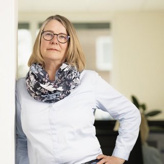 Selbstbewusste Frau posiert lächelnd in einem hellen Raum In einem hellen Raum lehnt eine lächelnde Frau mit blonden Haaren an einer Wand und trägt ein elegantes Outfit.