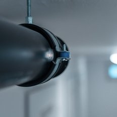 Nahaufnahme eines stabilen Rohres, das mit einer Metallklemme an der Decke montiert ist, im Hintergrund verschwommene Lichter.