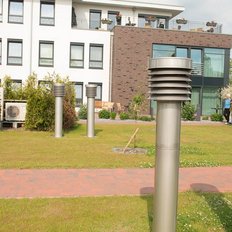 Eine ruhige Wohngegend mit einem modernen Gebäude, umgeben von gepflegten Pflanzen und mehreren vertikalen Lüftungseinheiten.