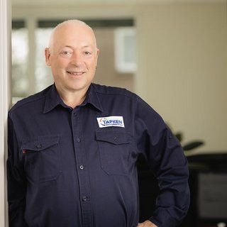 Freundlicher Angestellter mit Firmenlogo in modernem Büro Der Mann mit Glatze trägt ein Hemd mit dem Logo 'TAPKEN' und strahlt Freundlichkeit in einem hellen Raum aus.