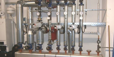 Metallische Rohrleitungen und Ventile, die an einer Wand montiert sind, zeigen eine industrielle Umgebung mit präzisen Messinstrumenten.