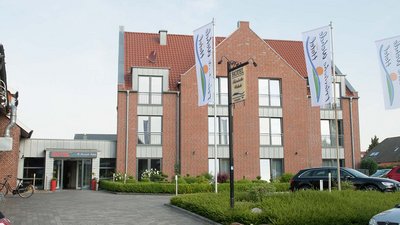 Ein einladender Hotelbereich mit einem klaren Eingang, umgeben von Pflanzen und einem Parkplatz, der für Gäste bereitsteht.