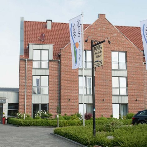 Ein einladender Hotelbereich mit einem klaren Eingang, umgeben von Pflanzen und einem Parkplatz, der für Gäste bereitsteht.