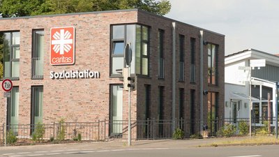 Ein helles, einladendes Gebäude mit dem Caritas-Logo, umgeben von einer grünen Landschaft und Verkehrsschildern.