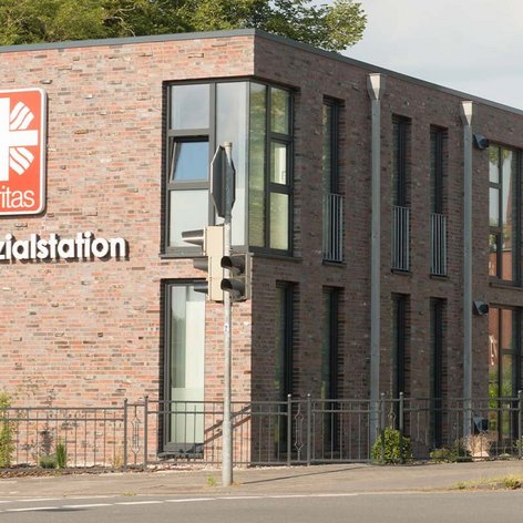 Ein helles, einladendes Gebäude mit dem Caritas-Logo, umgeben von einer grünen Landschaft und Verkehrsschildern.