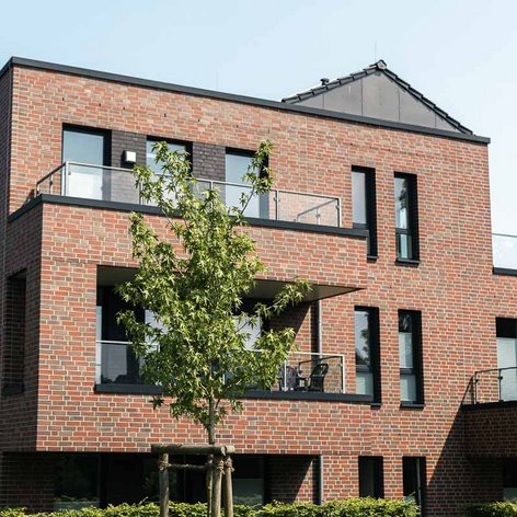 Das Gebäude zeigt eine zeitgenössische Architektur mit klaren Linien, großen Fenstern und einem begrünten Außenbereich.