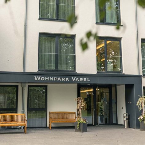Der Eingangsbereich des Wohnparks Varel zeigt moderne Architektur mit großen Fenstern und einladenden Holzbänken.