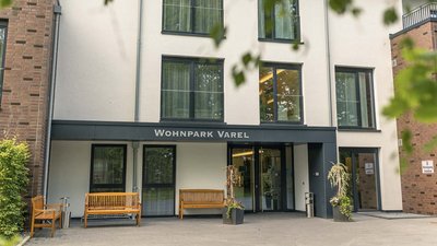 Der Eingangsbereich des Wohnparks Varel zeigt moderne Architektur mit großen Fenstern und einladenden Holzbänken.