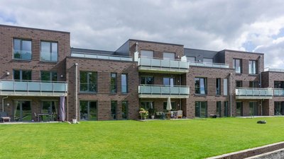 Moderne Wohnanlage mit mehreren Etagen, großen Fenstern und Balkonen, umgeben von einem gepflegten Rasen.