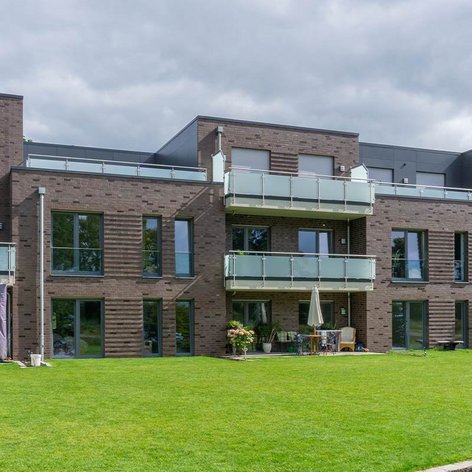 Moderne Wohnanlage mit mehreren Etagen, großen Fenstern und Balkonen, umgeben von einem gepflegten Rasen.