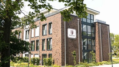 Das Gebäude, umgeben von Bäumen und Sträuchern, zeigt eine einladende Fassade mit einem Schild, das 'Wohnpark Varel' anzeigt.