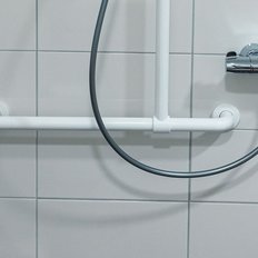 Eine moderne Duscharmatur mit einem flexiblen Schlauch und einem Handtuch in tiefrot hängt an einer weißen Wand.