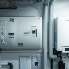 Eine moderne Heizungsanlage mit einem weißen Gehäuse und verschiedenen Rohren, die an der Wand montiert sind.