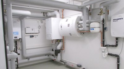 Ein technischer Raum mit verschiedenen Rohren und Heizgeräten, die an weißen Wänden montiert sind, sorgt für eine moderne Atmosphäre.