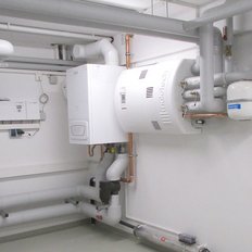 Ein technischer Raum mit verschiedenen Rohren und Heizgeräten, die an weißen Wänden montiert sind, sorgt für eine moderne Atmosphäre.