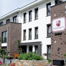 Die Fassade eines eleganten Hauses mit einem Schild, das den Namen 'Wohnpark Schortens' zeigt, vor einem blauen Himmel.