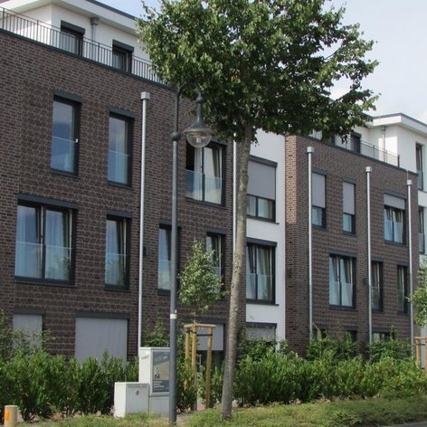 Stilvolle Wohnanlage mit einer Mischung aus Backstein- und Putzfassade, ergänzt durch moderne Fenster und Pflanzen.