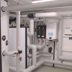 Ein technischer Raum mit zahlreichen Rohren und Heizgeräten, die an weißen Wänden montiert sind, sorgt für eine moderne Atmosphäre.
