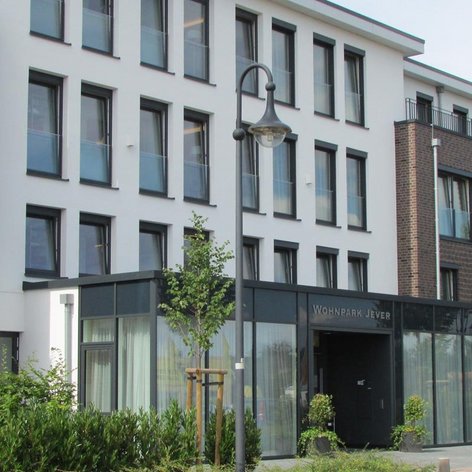 Der Eingangsbereich des Wohnparks Jever zeigt eine stilvolle Glasfront und eine einladende Atmosphäre mit Pflanzen.