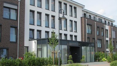 Der Eingangsbereich des Wohnparks Jever zeigt eine stilvolle Glasfront und eine einladende Atmosphäre mit Pflanzen.