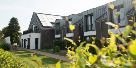 Eine moderne Wohnanlage mit begrünten Gärten und Terrassen, umgeben von Bäumen und Sträuchern, strahlt Ruhe und Gemütlichkeit aus.