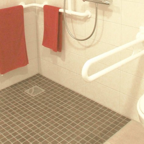 Ein barrierefreies Badezimmer mit Haltegriffen, einem WC und roten Handtüchern an der Wand, das eine sichere Nutzung ermöglicht.