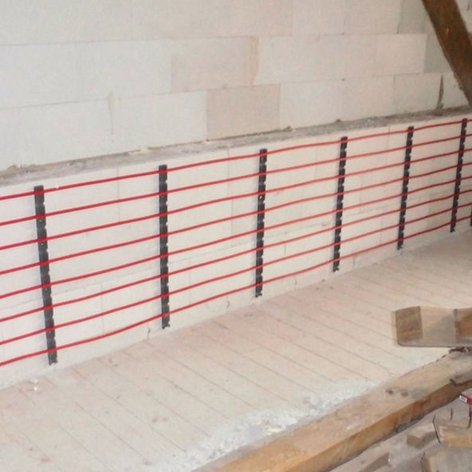 Eine unvollendete Wand mit roten Heizungsrohren, die an einer weißen Mauer montiert sind, umgeben von Holzresten.