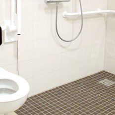 Ein barrierefreies Badezimmer mit einer Toilette, Haltegriffen und einem Duschbereich, der für Menschen mit Mobilitätseinschränkungen geeignet ist.