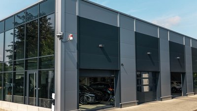 Ein modernes, graues Gebäude mit großen Fenstern, das mehrere Autos in der Garage zeigt, umgeben von Bäumen.