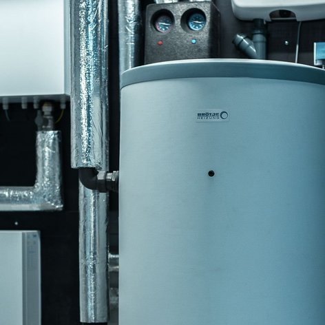 Ein großer, runder Heizungsboiler steht in einem modernen Heizungsraum, umgeben von silbernen Rohren und Geräten.