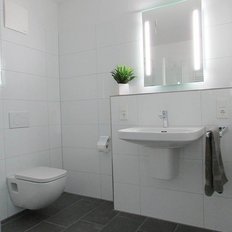 Ein modernes Badezimmer mit weißen Fliesen, einem Waschbecken und einem eleganten Spiegel mit LED-Beleuchtung.