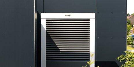 Das Bild zeigt eine stilvolle Wand mit einem horizontalen Lüftungsgitter, das von einem klaren blauen Himmel beleuchtet wird.