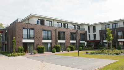 Moderne Wohnanlage mit mehreren Etagen, begrünten Außenbereichen und einem Bewohner auf dem Balkon im Hintergrund.
