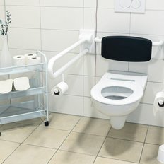 Ein barrierefreies Badezimmer mit einem Toilettenstuhl, Haltegriffen und einem kleinen Regal für Toilettenartikel.